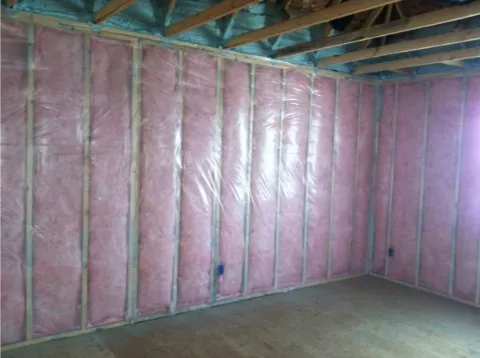 Interior wall with pink fiberglass insulation and covered with vapor barrier.